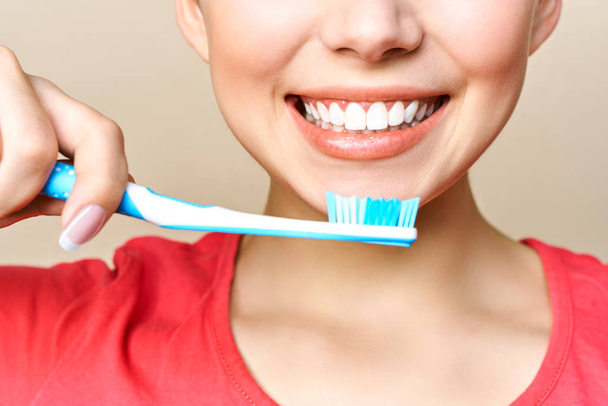 Jonge mooie vrouw is bezig met het schoonmaken van tanden. Mooie glimlach gezonde witte tanden. Een meisje houdt een tandenborstel. Het concept van mondhygiëne. Promotionele afbeelding voor een stomatologie, tandheelkundige kliniek - Foto, afbeelding