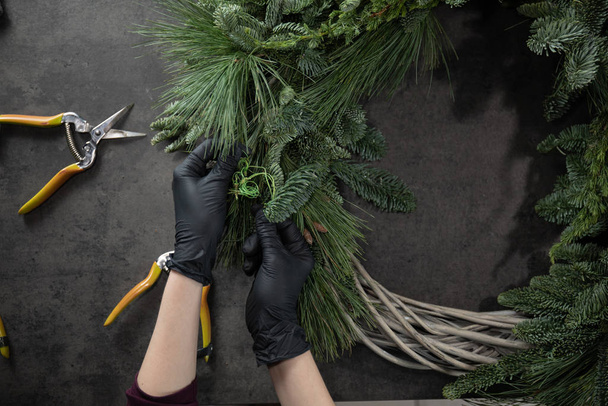 Vista superior de las manos floristas haciendo corona de Navidad con ramas de abeto en la mesa
 - Foto, Imagen