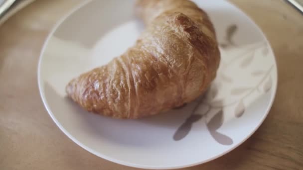 Francouzské croissanty na talíři, zblízka. Záběry ze skladu. Lahodný čerstvě upečený křupavý croissant ležící na talíři na dřevěném podkladu stolu. - Záběry, video