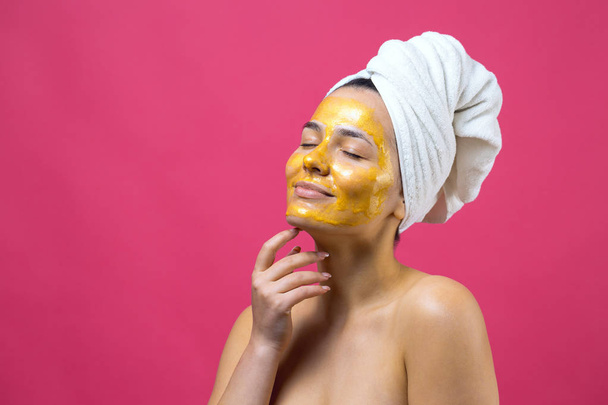 Retrato de belleza de mujer en toalla blanca en la cabeza con máscara nutritiva de oro en la cara. Limpieza de la piel ecológico cosmético spa relajante concepto
. - Foto, Imagen