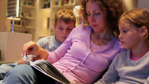 Niño y niña con su madre sentarse en el sofá y leer libro
 - Imágenes, Vídeo
