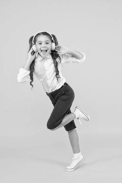 A perfect song for active child. Happy little girl moving active to music. Active schoolchild running to school on yellow background. Active and energetic small kid listening to music in earphones - Foto, Imagem