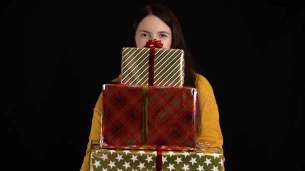 黒を背景にギフトボックスを持つ若い女性。ハッピーニューイヤー、メリークリスマス、バレンタインデー、誕生日のための白いリボンとギフトボックス. - 映像、動画