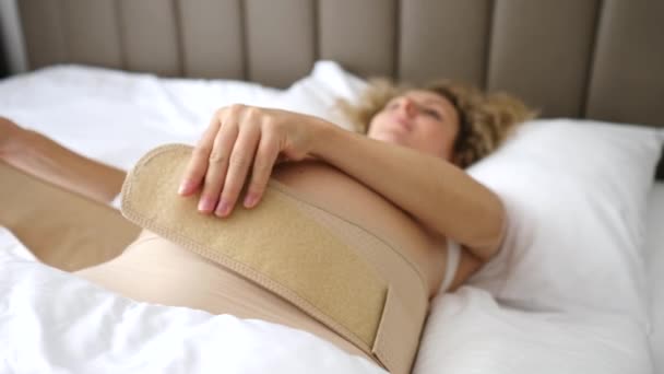 Zwangere vrouw ligt op bed en zet op Abdominale Ondersteuning Bandage. Moederschapsondersteunende producten. - Video