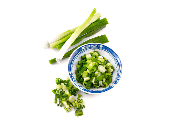 chopped spring onion, scallions, in a blue dish on white background - Фото, изображение