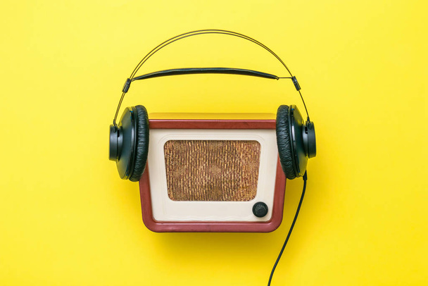 Μαύρα ακουστικά με σύρμα και vintage ραδιόφωνο σε κίτρινο φόντο. Vintage τεχνική. - Φωτογραφία, εικόνα