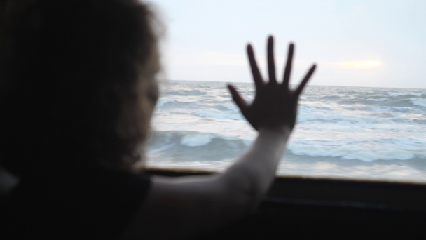 Mujer viaja en tren con la mano en la ventana diciendo adiós al mar
 - Metraje, vídeo