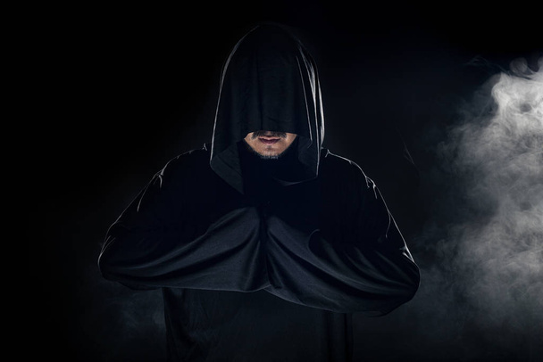 Man dressed in a dark robe looking like a cult leader on a smoky or foggy background.  He looks like a creepy evil villain - Foto, Bild