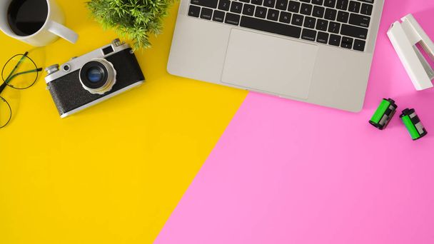 Widok góry nowoczesnego miejsca pracy z laptopem i materiałami biurowymi na różowym i żółtym tle biurka - Zdjęcie, obraz