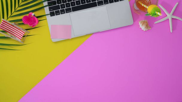 Draufsicht auf farbenfrohen Sommer-Arbeitsplatz mit Laptop und Bürobedarf auf rosa und gelben Schreibtischhintergrund - Foto, Bild