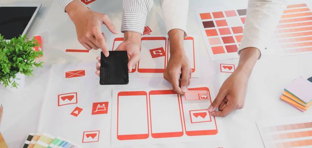 Обрезанный снимок молодой команды графических дизайнеров UX, работающих вместе над шаблоном смартфона
  - Фото, изображение