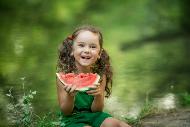 Tyttö hiukset punottu syö vesimelonia lähellä järveä
 - Valokuva, kuva