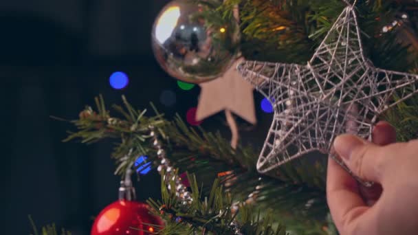 Een vrouw hangt kerstversiering op kerstboom tak blad, close-up schot, met glinsterende tekenreeks Led lamp in de donkere zwarte achtergrond. - Video