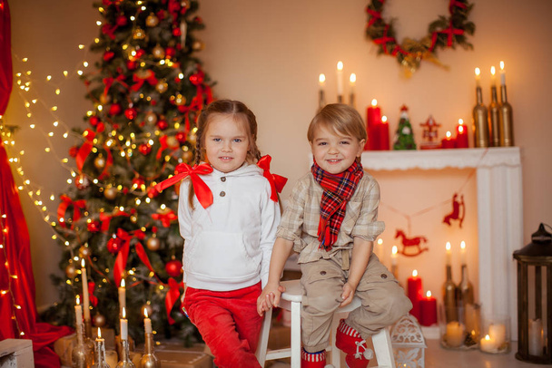 Beautiful kids brother and sister on kami background with Christmas lights and Christmas tree decorated with garland - Photo, Image