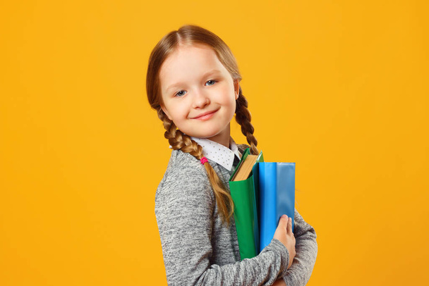 Closeup portrait of little girl schoolgirl on yellow background. The child holds textbooks. The concept of education and school - Zdjęcie, obraz