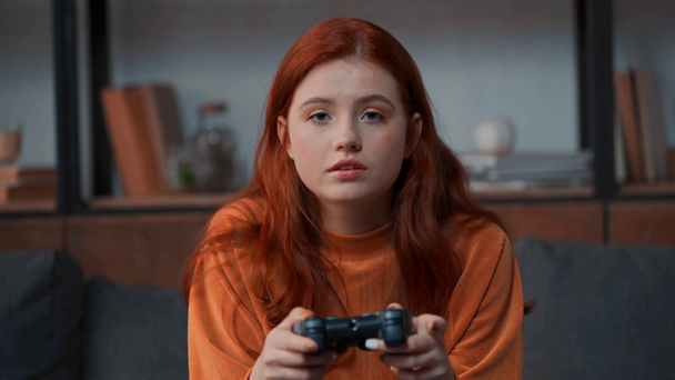 KYIV, UKRAINE - NOVEMBER 8, 2019: attentive redhead teenage girl playing video game - Séquence, vidéo