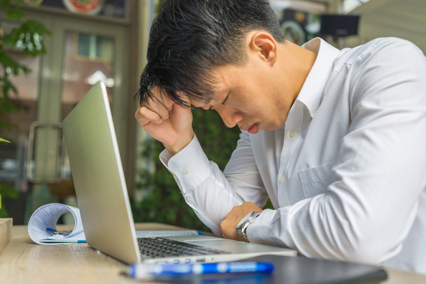 Frustrated young businessman working on laptop and paperworks - 写真・画像