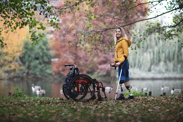 Ein behindertes Mädchen ohne Beine steht auf Prothesen neben einem Rollstuhl. - Foto, Bild
