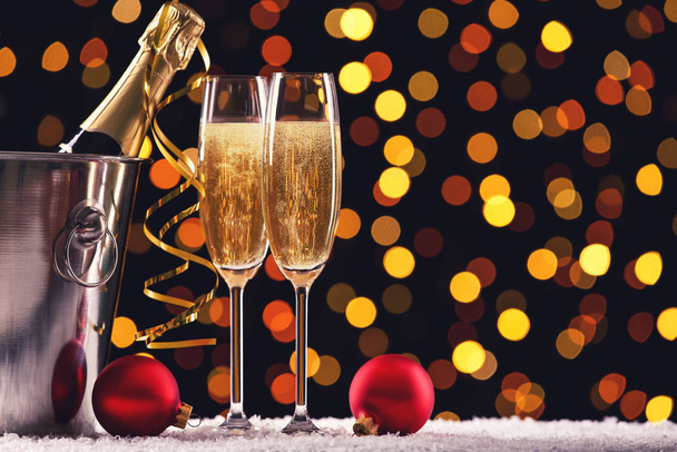 Bottle and glasses of champagne with red baubles on blurred lights background - Photo, image