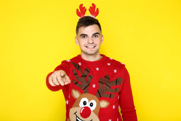 Beautiful man wearing red christmas sweater and horns on yellow background - Zdjęcie, obraz