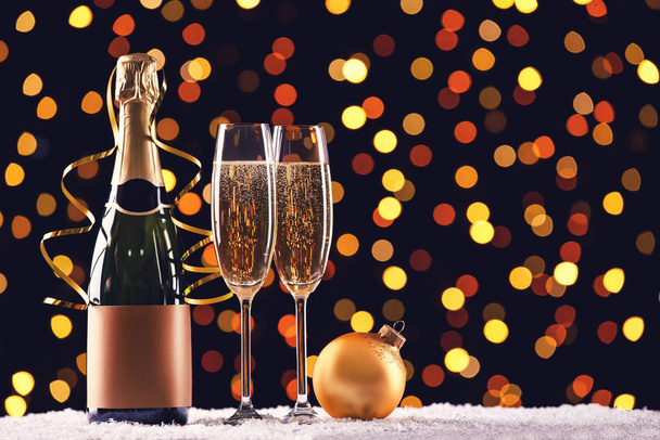 Bottle and glasses of champagne with bauble on blurred lights background - Foto, immagini