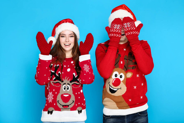 Beautiful man and woman wearing christmas sweaters, gloves and santa hats on blue background - Foto, Imagem