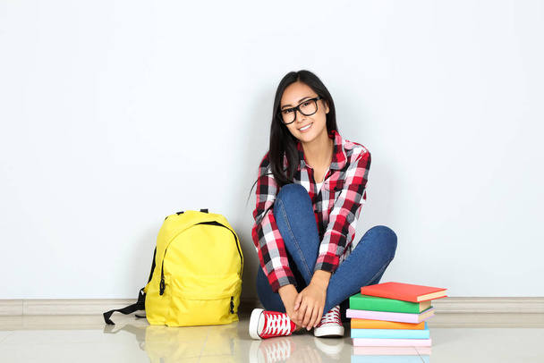 Young woman sitting with books and backpack on grey background - Foto, Bild