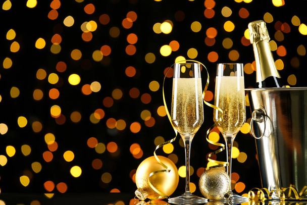 Fles en glazen champagne met kerstballen op wazig licht achtergrond - Foto, afbeelding