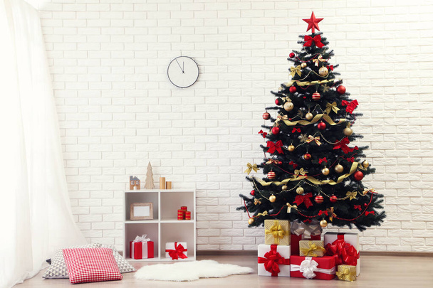 Christmas fir tree with ornaments and gift boxes standing at home near white brick wall - Valokuva, kuva