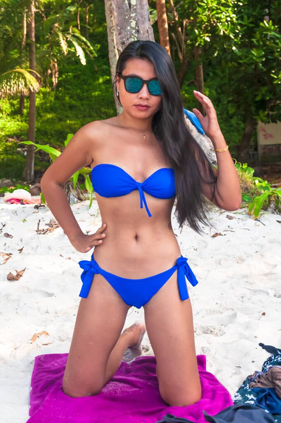 Vertical shot of a beautiful Asian female model in a blue bikini kneeled with a confident look - Zdjęcie, obraz