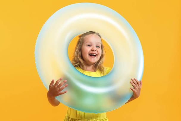 Portrait of a happy child little girl in a dress with a swimming ring on a colored yellow background. Vacation concept - Photo, Image