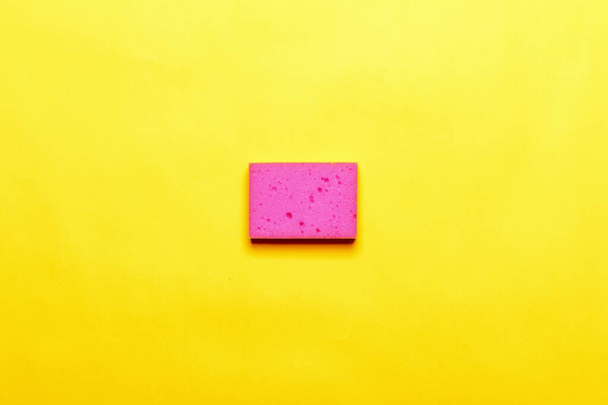 Colored pink sponge on a yellow background. Top view - Zdjęcie, obraz