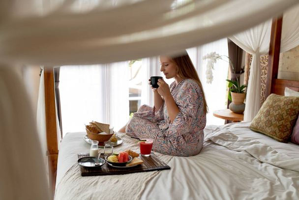 Mujer joven en habitación de hotel luminosa comiendo saludable descanso vegetariano
 - Foto, Imagen