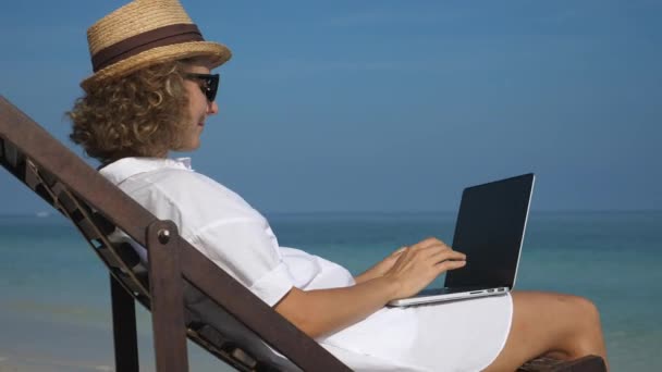 Frau, die am Strand am Meer am Laptop arbeitet. Fernarbeit, freiberufliches, digitales Nomadenkonzept. - Filmmaterial, Video