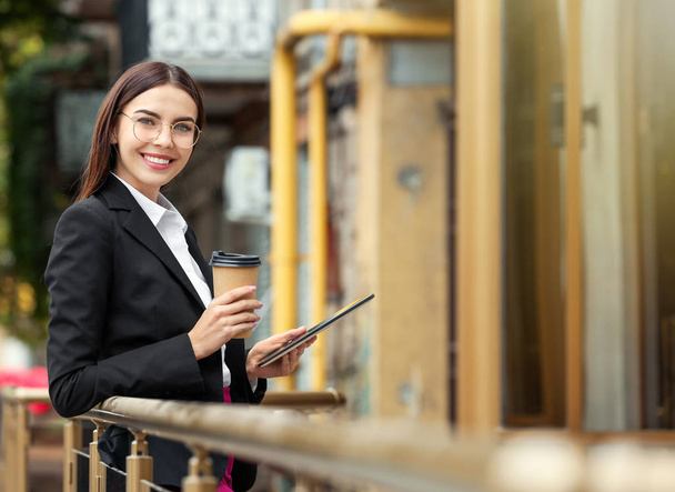 Beautiful young businesswoman with coffee and tablet computer outdoors - Photo, Image