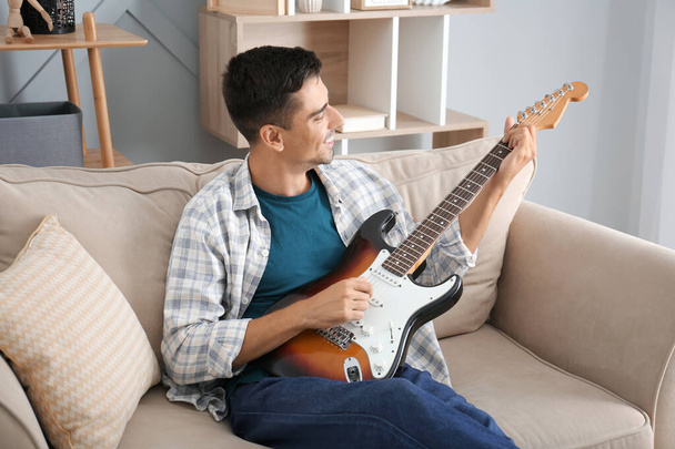 pohledný muž hraje doma na kytaru - Fotografie, Obrázek
