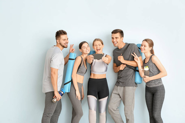 Ομάδα ατόμων με στρώματα γιόγκα λήψη selfie κοντά σε έγχρωμο τοίχο - Φωτογραφία, εικόνα