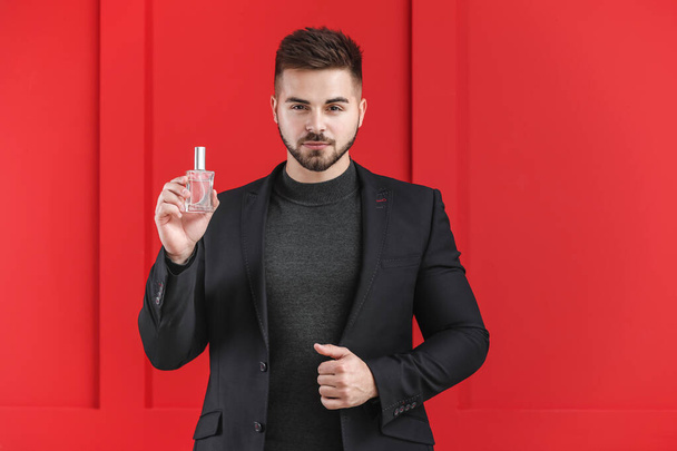 Handsome young man with bottle of perfume on color background - Foto, imagen