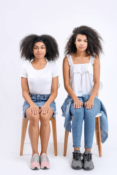 Portrait of young African-American women sitting on chairs against white background - Fotografie, Obrázek