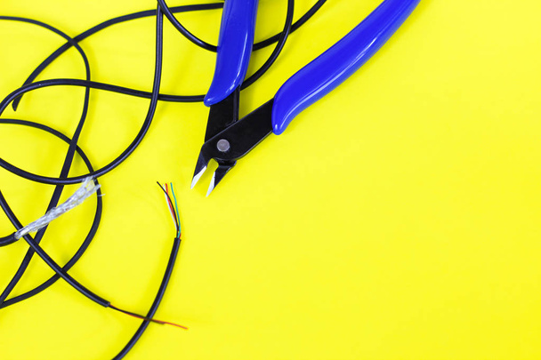 tangled charger wires. Black wire on a yellow background with blue nippers - Photo, Image