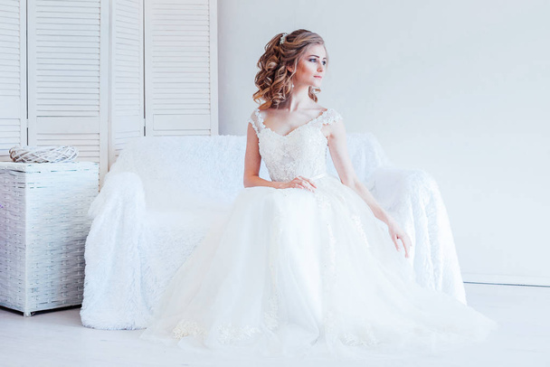 beautiful bride sitting on a white couch in wedding dress - Zdjęcie, obraz