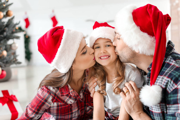 Vanhemmat suutelevat tytärtään kotona jouluaattona.
 - Valokuva, kuva