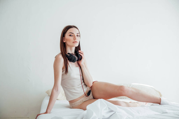 Nainen brunette iso kuulokkeet istuu sängyllä
 - Valokuva, kuva