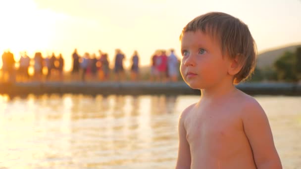 Pikkulapsi seisoo meren rannalla auringonlaskun aikana. Mielenterveys. Lasten psykologiaa. Kasvojen ilme. Erityinen ilme. Nuori turisti lähellä merta. Loma lapsen kanssa. Lapsuuden tausta
 - Materiaali, video