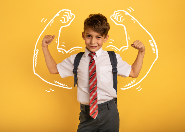 Young boy student acts like a muscled man. Yellow background - Photo, Image