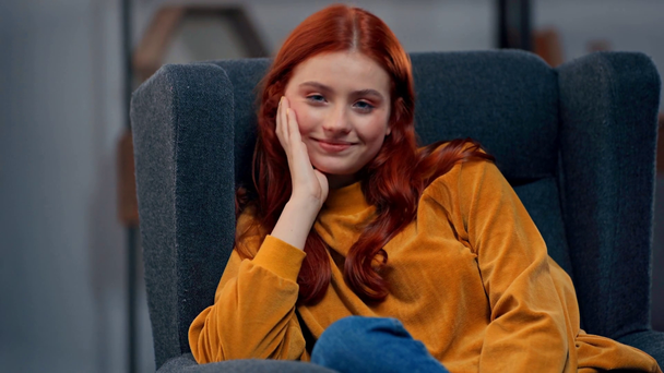 Pozitif kızıl saçlı genç kadın koltukta oturuyor. - Video, Çekim