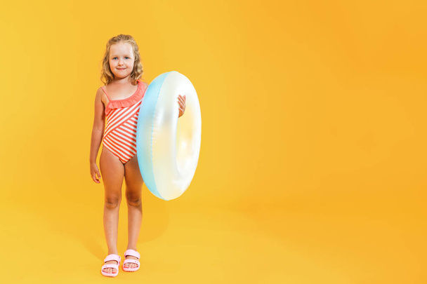 Portrait of a happy child little girl in a bathing suit with a swimming ring on a colored yellow background. Vacation concept - Foto, afbeelding