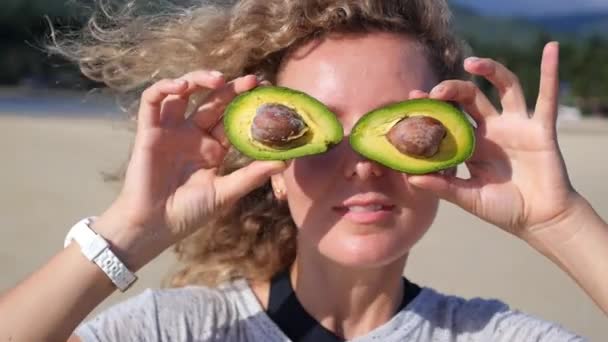Wesoła kobieta robi oczy awokado na plaży - Materiał filmowy, wideo