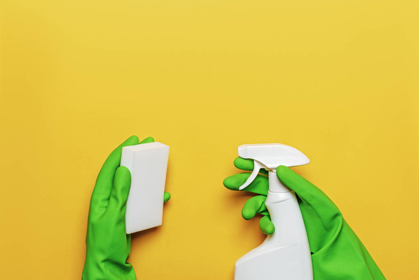 Worker's hands in rubber protective gloves with a sponge and spray bottle on a yellow background. The concept of cleaning, taking care of the house - Фото, изображение