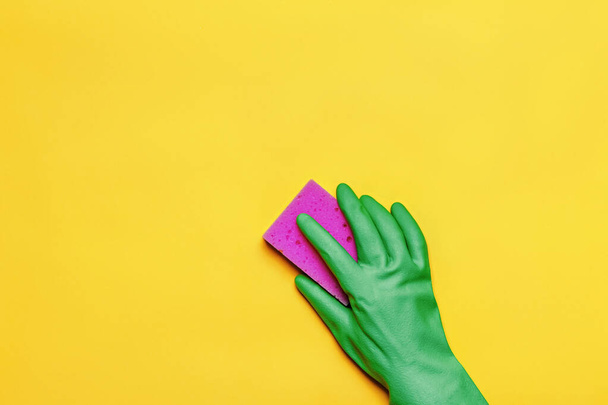 A hand in a rubber protective glove with a pink sponge on a yellow background. Cleaning concept - Foto, Imagem